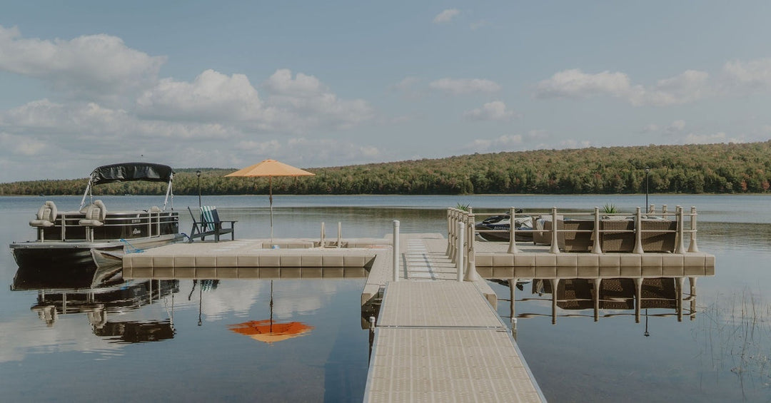 Floating dock with seating area and boat tied alongside on a calm lake, with forested shoreline under a clear sky.