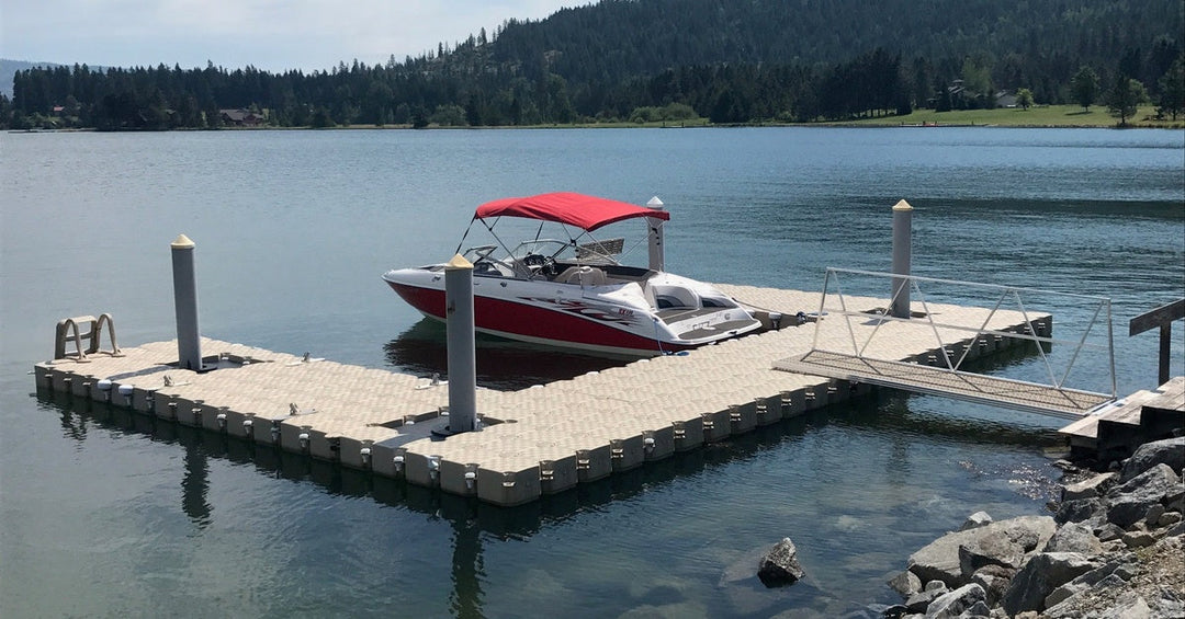 A modular floating dock with a red canopy boat sits on a calm lake, connected to shore by a narrow gangway.