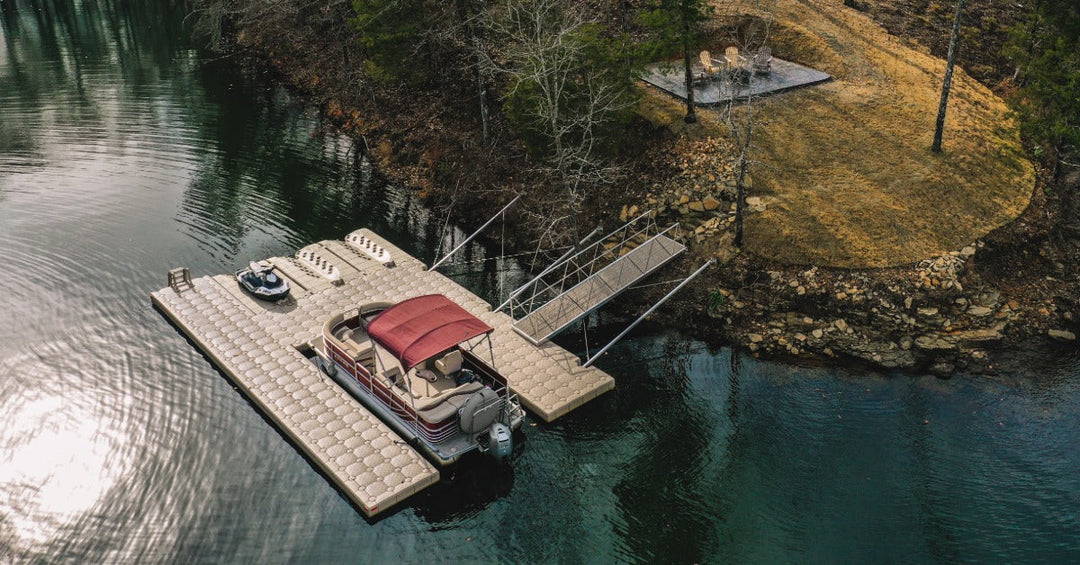 A floating dock holding a pontoon boat connected by a walkway to a wooded shoreline beside rippling water.